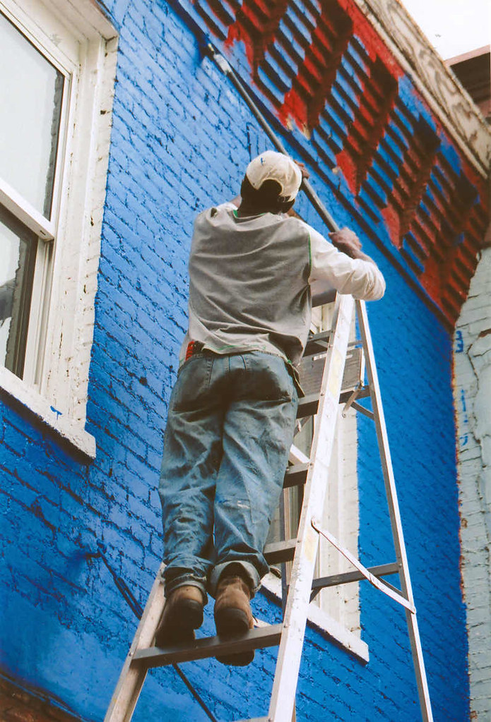 Exterior wall repaint in progress from a ladder